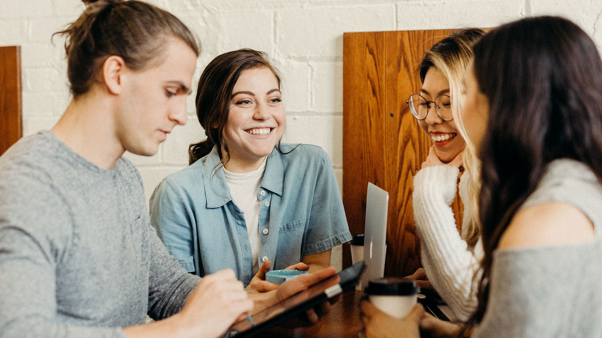 Four young adults smiling and drinking coffee one male is checking a device